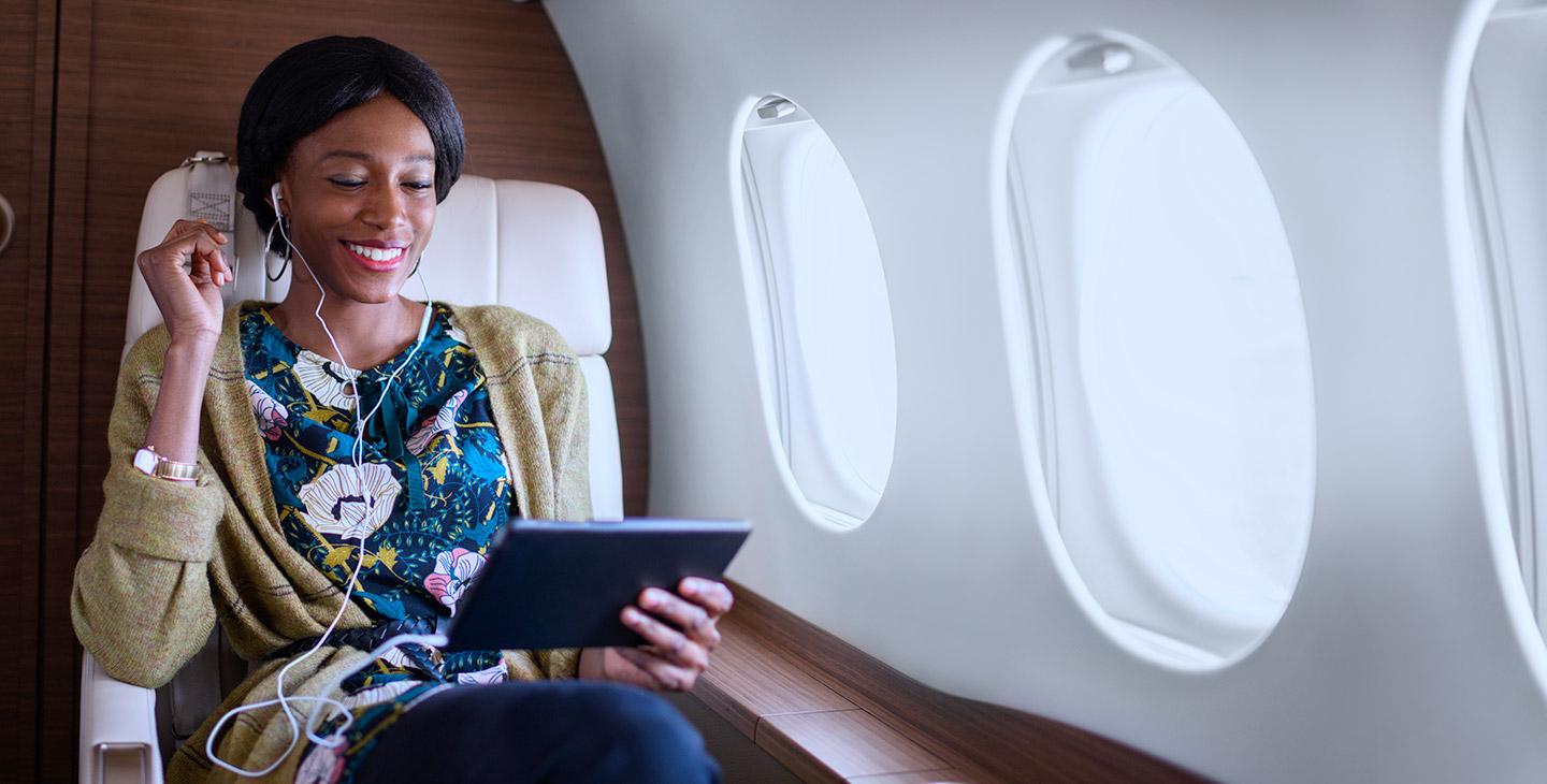 Woman wearing a floral shirt wearing a headset connected to a tablet, enjoying jet inflight entertainment on a private jet