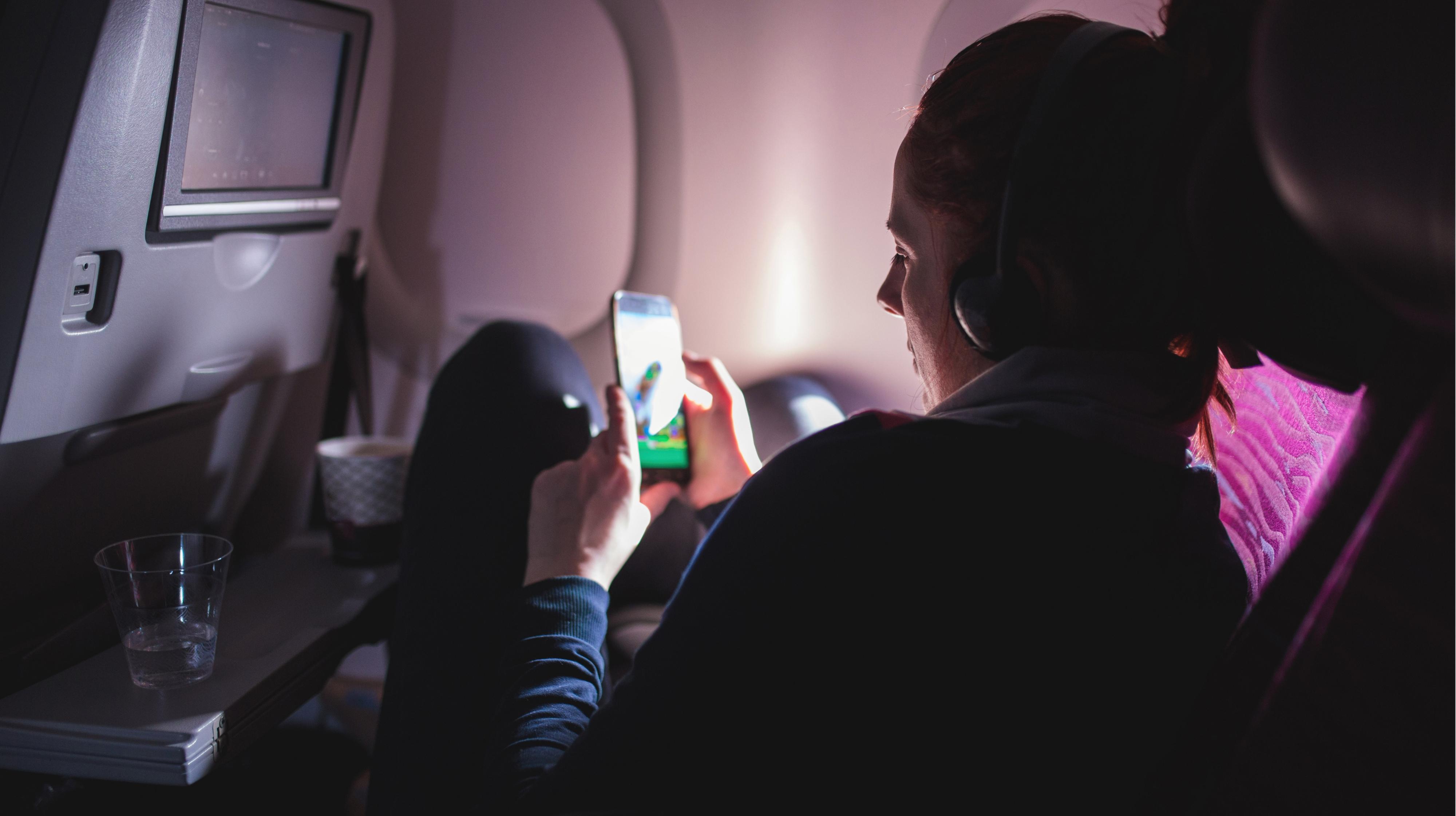 一个戴着耳机的人蜷缩在飞机座位上，看着手机屏幕上的东西. 
